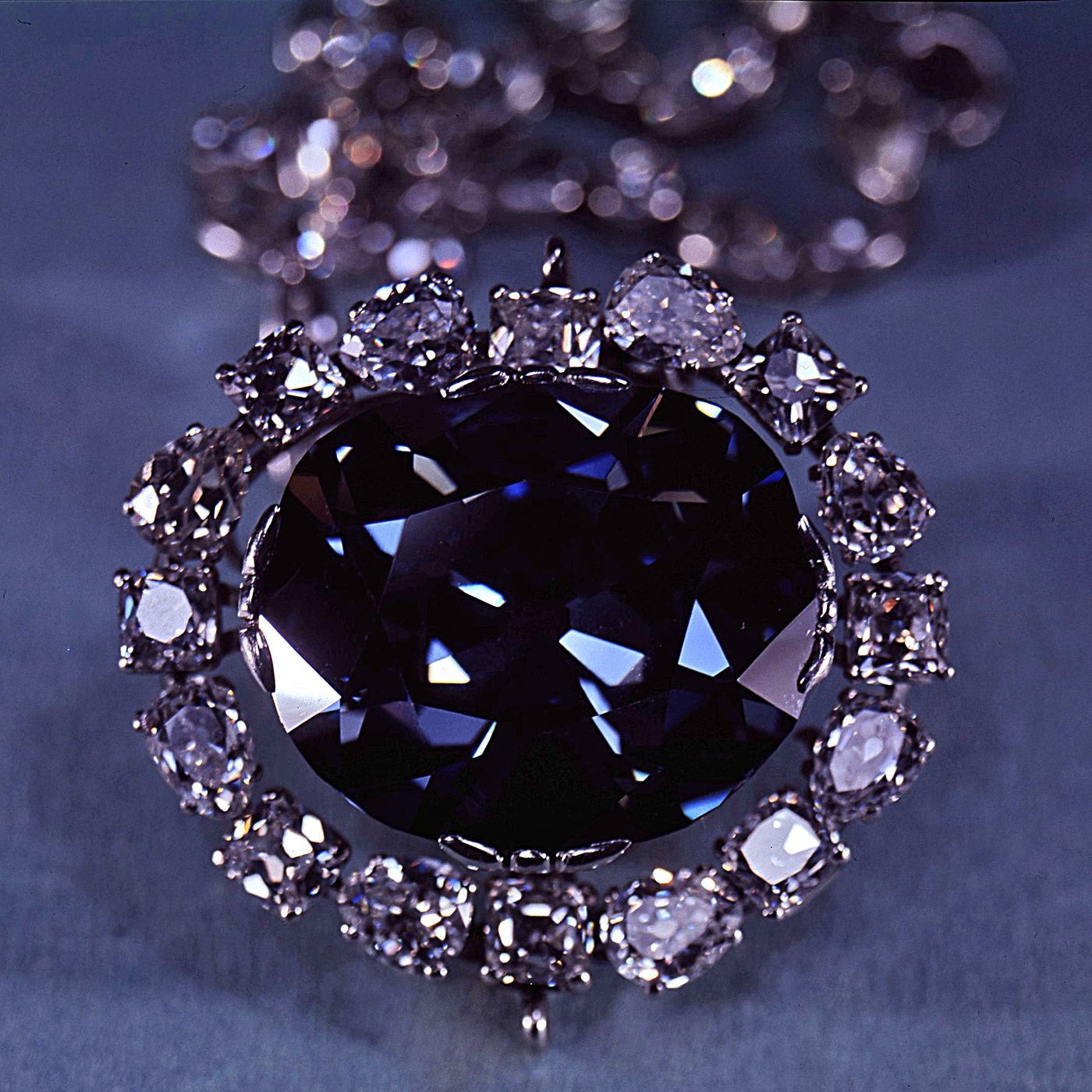 A deep blue diamond surrounded by white diamonds, photographed on grey cloth.