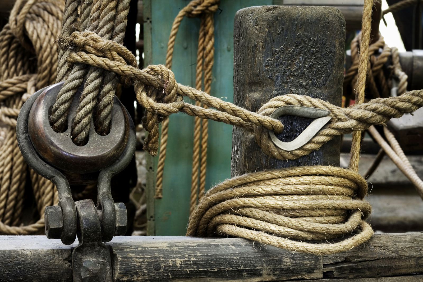 Rope coiled on a wooden belaying pin beside a rusted shackle.