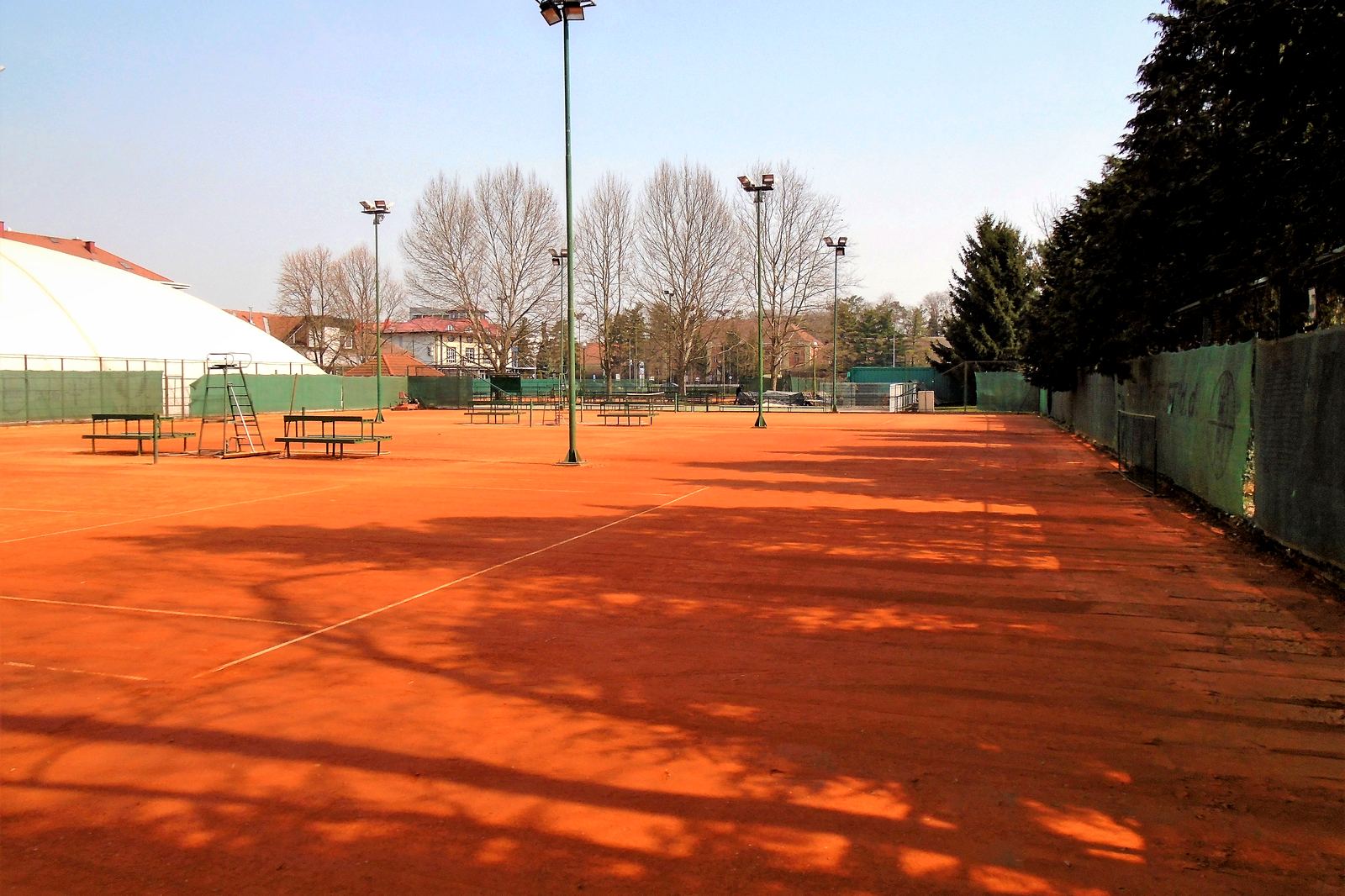 An empty clay tennis court in low sun, its lines freshly drawn.